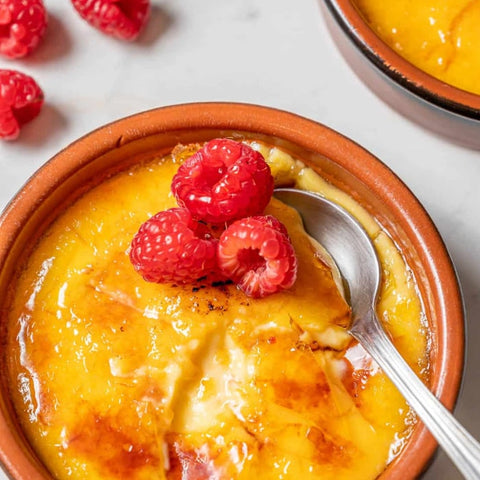 Crema Catalana with raspberries in a terracotta dish on a white background