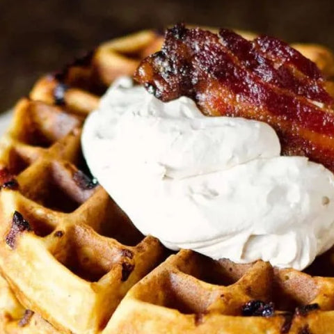 Waffle topped with maple whipped cream and bacon on a dark background