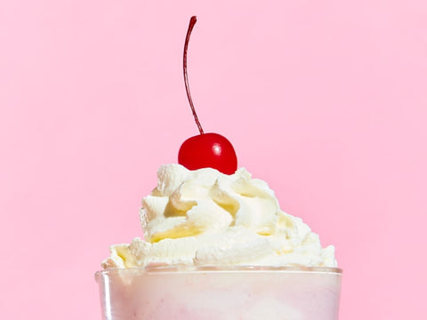 A milkshake with homemade whipped cream on top in front of a pink background