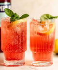 Two cocktails with basil leaves and lemon slice in a glass, Campari bottle in the background