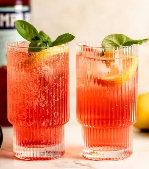 Two cocktails with basil leaves and lemon slice in a glass, Campari bottle in the background