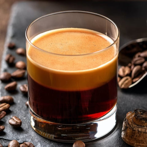 Glass of layered espresso cocktail with coffee beans on a dark surface