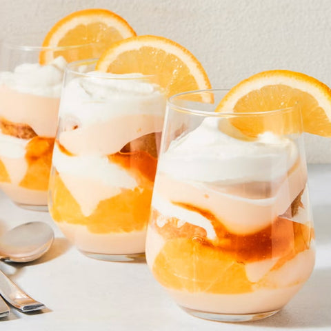 Three glasses of dessert with orange slices and whipped cream on a light background