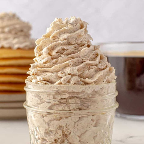 Jar of cinnamon whipped cream with pancakes and coffee in the background