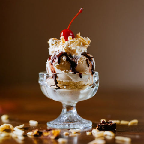 Glass dish with ice cream sundae topped with a cherry and peanuts on a wooden surface