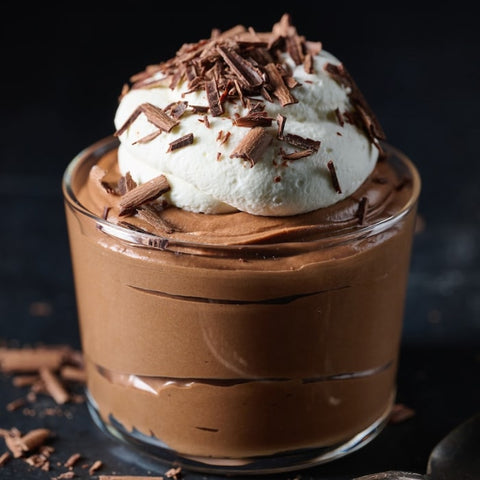 Chocolate mousse with whipped cream and chocolate shavings in a glass jar on a dark background