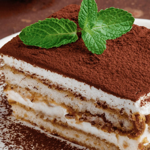 Slice of layered Tiramisu with cocoa powder and mint leaves on a plate