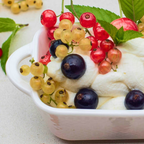 Lemon cheesecake mousse with fresh berries in a white container on a light background