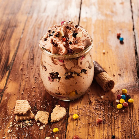 Glass jar filled with Nutella mousse on a wooden surface with cookies and candies.