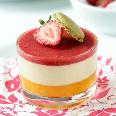 Layered dessert with strawberry on top, served in a glass bowl on a floral napkin.