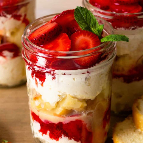 Strawberry shortcake in a jar with layers of cream and fruit on a wooden surface.