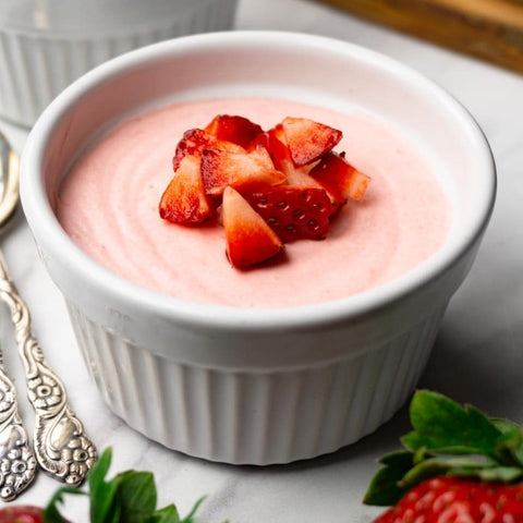 White ramekin filled with pink strawberry mousse topped with sliced strawberries on a light gray surface.